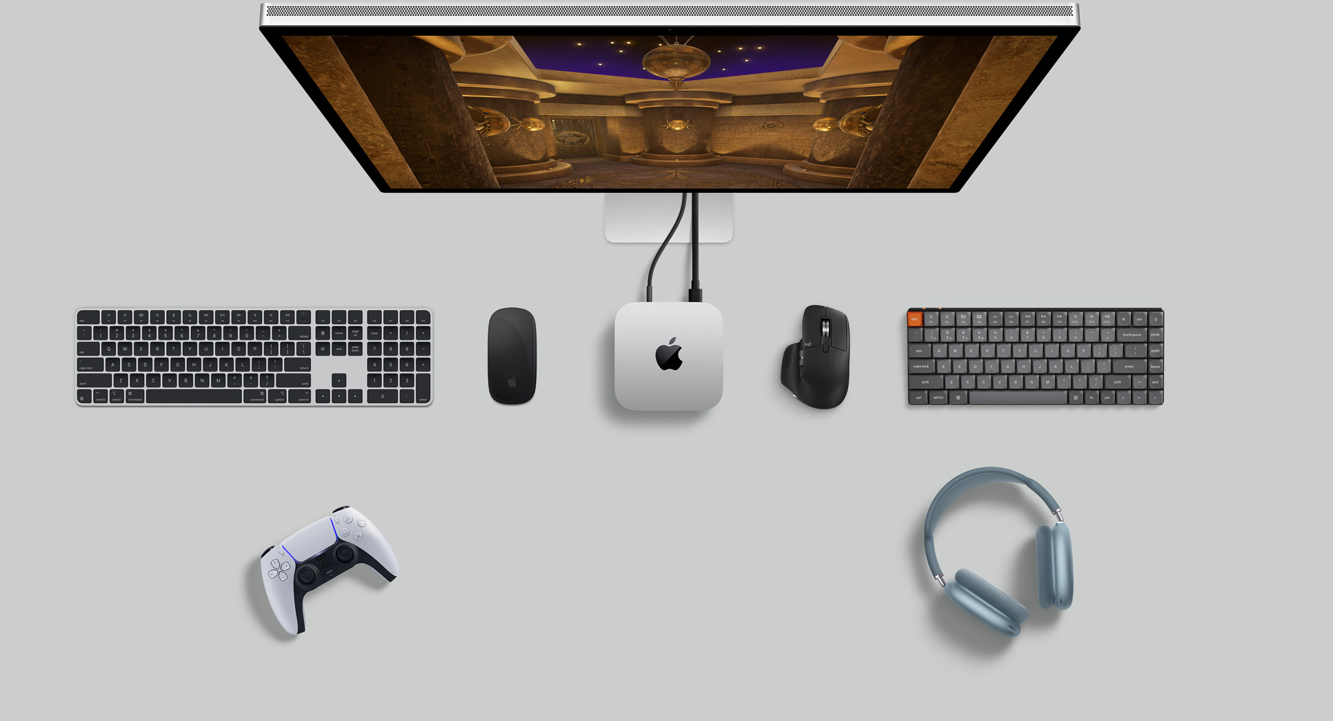 Изглед отгоре на сребърен Mac mini в комбинация с дисплей, безжични клавиатури, безжична мишка, гейминг контролер и AirPods Max