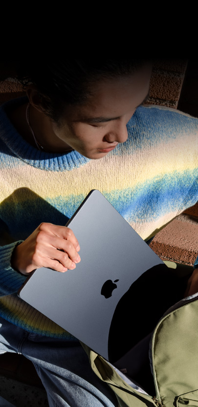 Eine Person steckt ein 15" MacBook Air in Mitternacht in einen Rucksack.