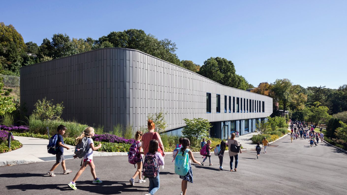 children walk downhill by the whale-like Upper Learning Building on a sunny day