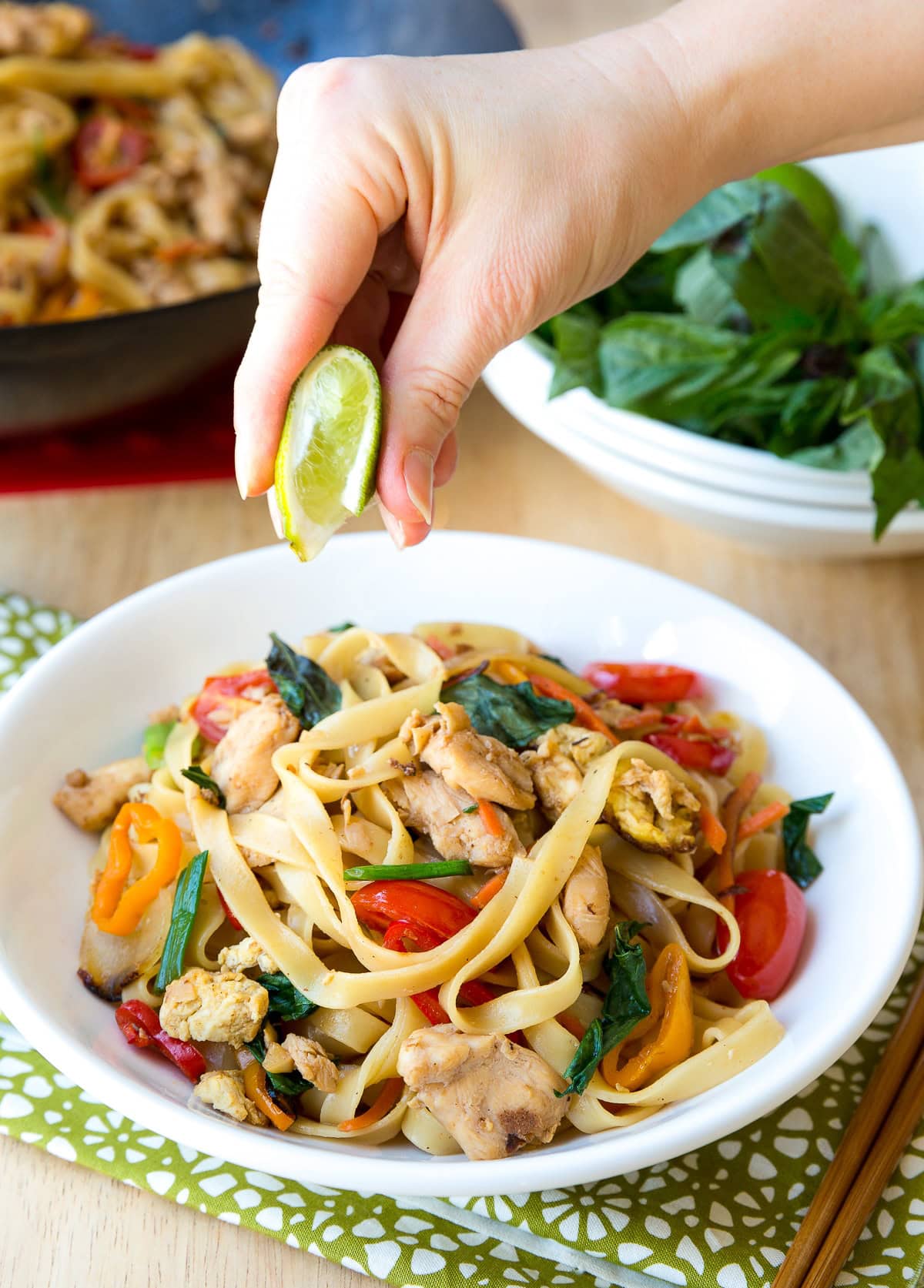 Hand squeezing lime onto drunken noodles in a bowl. 