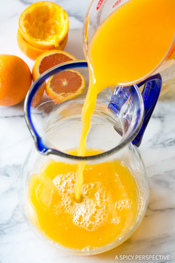 Fresh squeezed orange juice being poured into a glass pitcher for orangeade recipe