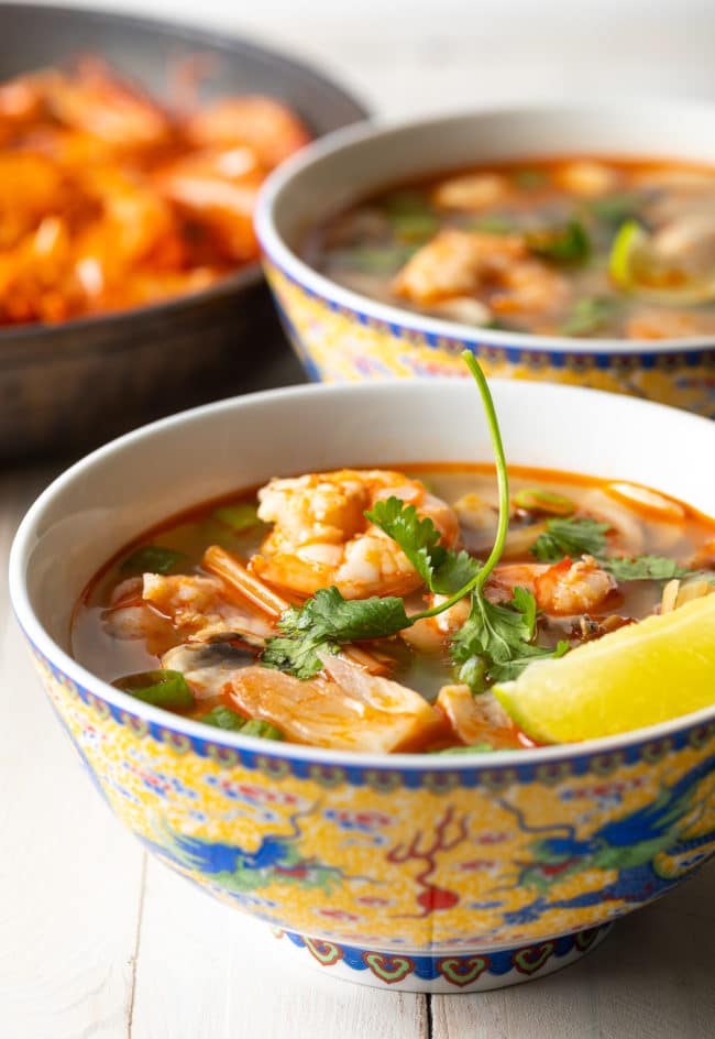 Two bowls of Thai hot and sour soup topped with cilantro and lime wedge. 