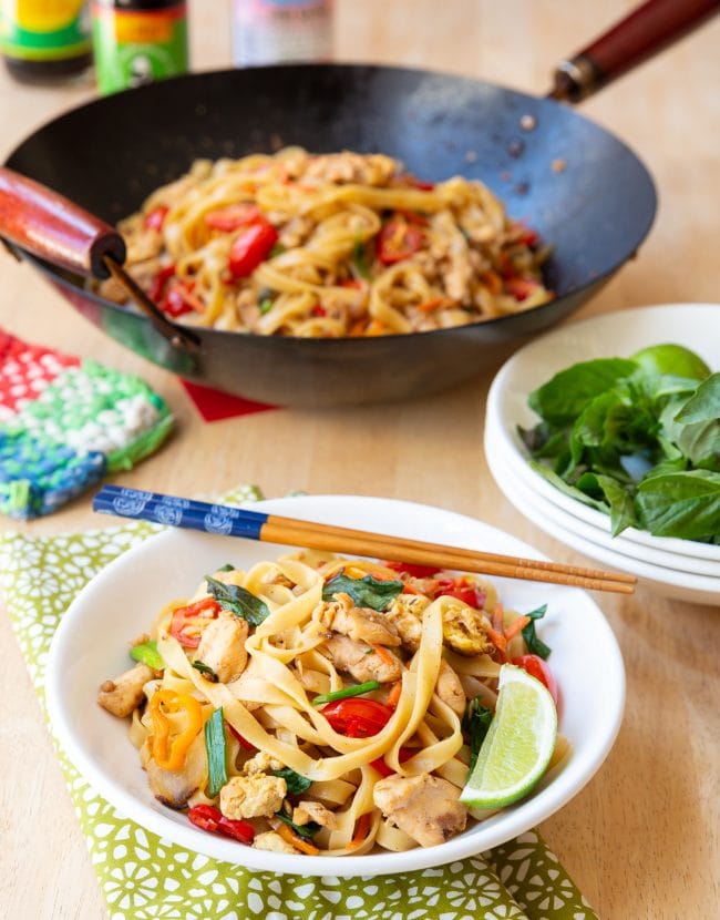 Drunken noodles served in a bowl with chopsticks on the side and more drunken noodles in the background. 