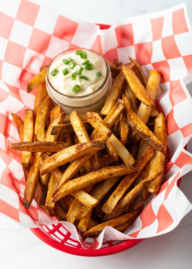 Top down view Cajun french fries in a white and red checkerboard container, with ramekin of dipping sauce.