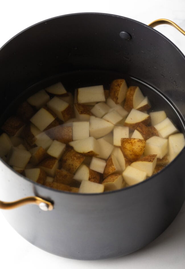 Large black pot with diced potatoes covered in water.