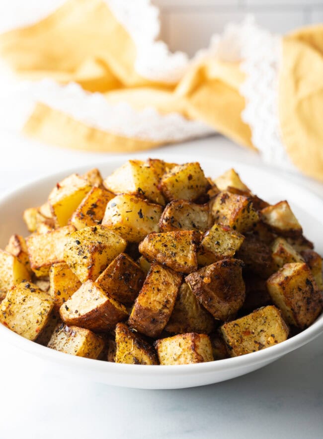 Close view cubed fried potatoes in a white bowl.