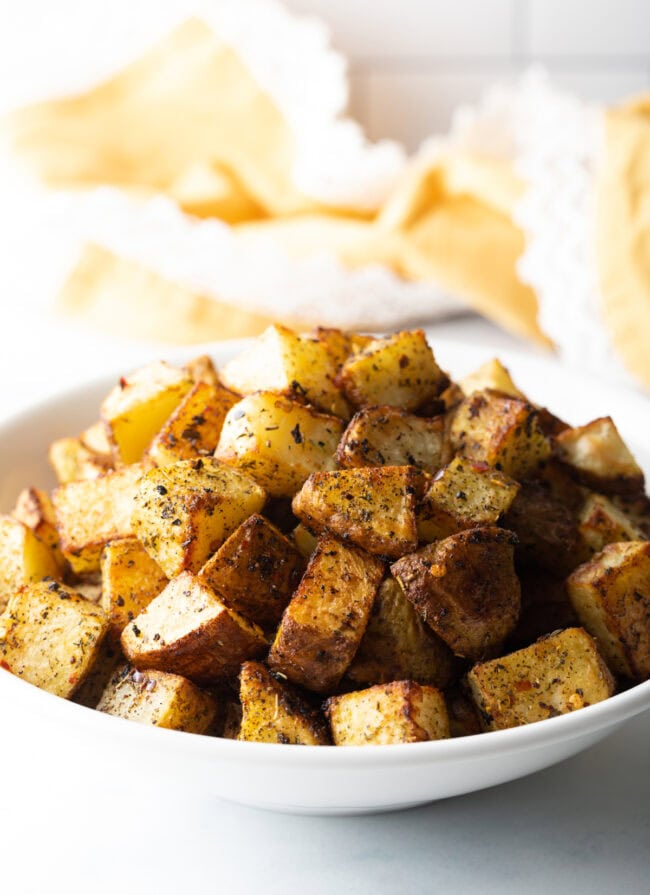 Cubes of roasted seasoned russet potato in a white bowl.