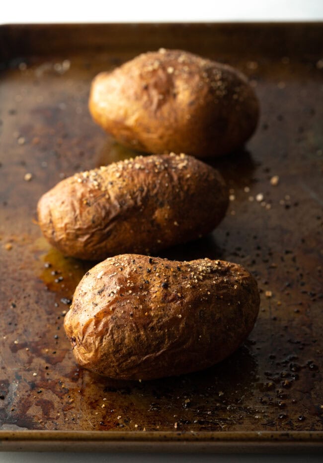 Three baked potatoes on a baking sheet.