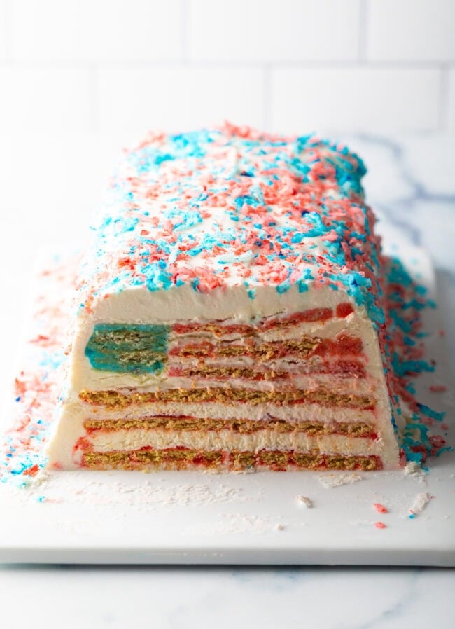 White rectangular icebox cake covered with red and blue coconut flakes. Cake is cut in the middle to show the inner American flag design.