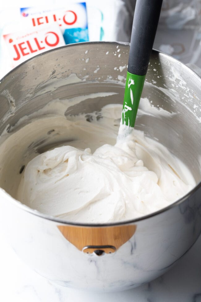 Freshly made whipped cream in a metal bowl with green spatula.