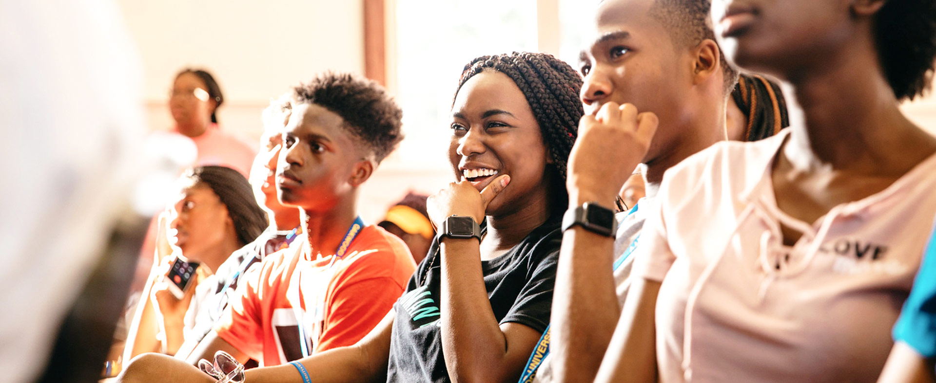 A diverse group of young people sits attentively in a bright room at Oakwood University. One person smiles broadly while others look focused, suggesting an engaging presentation or discussion.