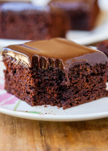 A slice of homemade chocolate ganache cake on a plate missing a bite.