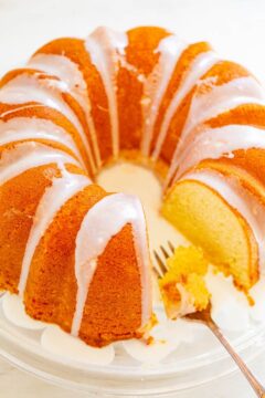 A sliced lemon bundt cake with white glaze on a glass plate with a fork.