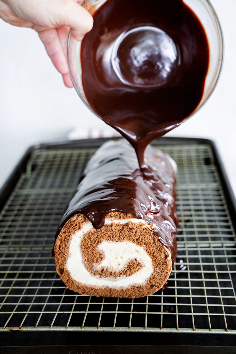 pouring homemade dark chocoalte ganache over ice cream roll cake on a wire rack set over a baking sheet