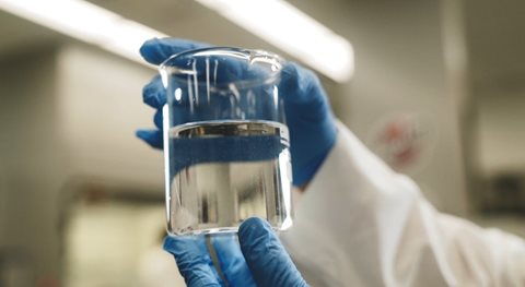 two gloved hands holding a beaker