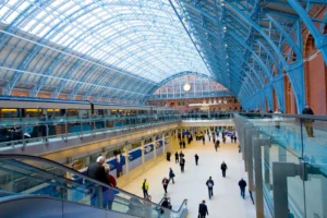 Travelers walk through the (concourse, terminal, platform, station). View down the length of the curve roof of the Barlow shed.