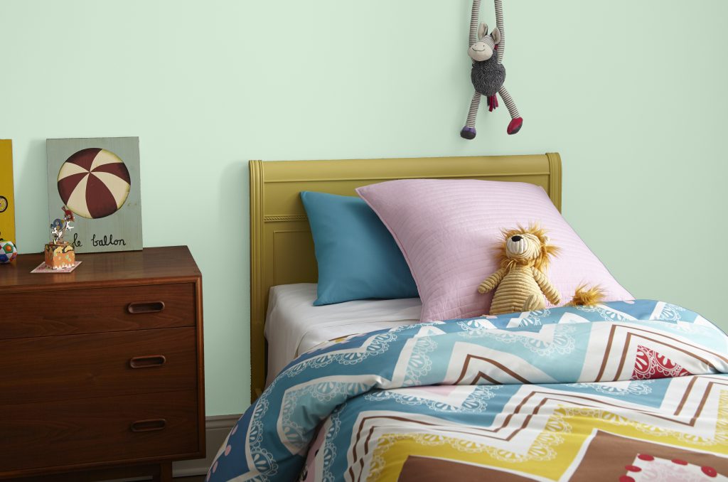 A child's bedroom showcasing a lgiht green wall, classic furniture and stuffed animal toys in bold colors 