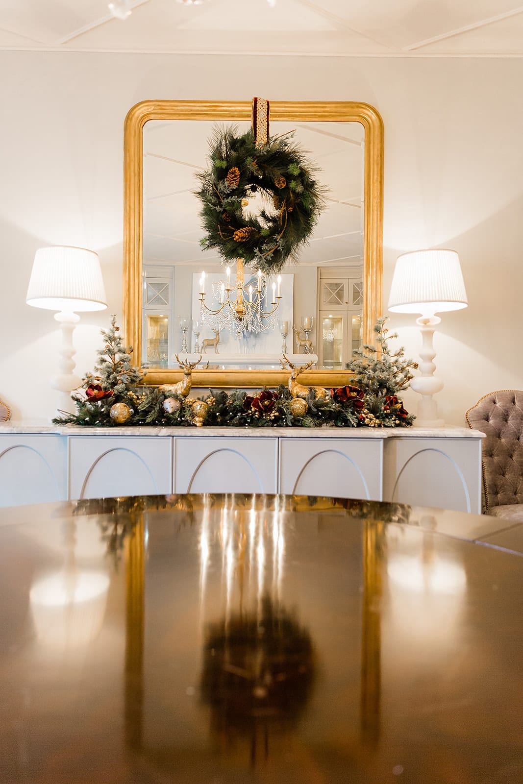 Glamorous dining room christmas table with gold ornate mirror in dining room with holiday wreath hanging from mirror. White Currey and Company marble lamps and Frontgate holiday decor in Atlanta blogger BlueGrayGals home.