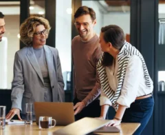 Four coworkers look at a laptop as they discuss their corporate matching gifts program