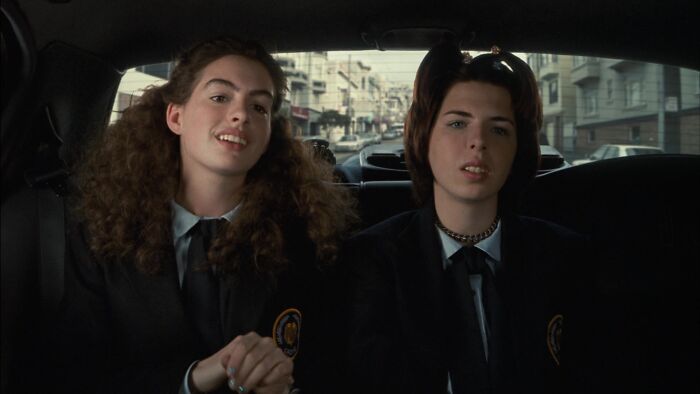 Two iconic best friend duos sitting in the backseat of a car, wearing black school uniforms.