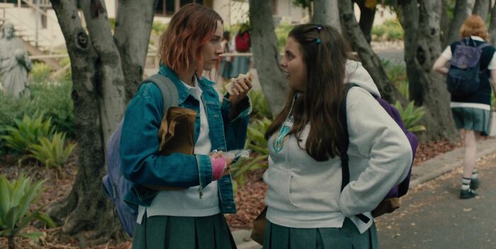 Two best friends talking in school uniforms, standing outdoors among trees, showing iconic friendship dynamics.