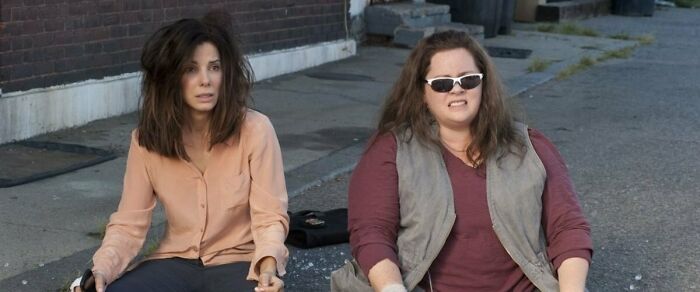 Two iconic best friend duos sitting on a city street, wearing casual outfits and looking surprised.