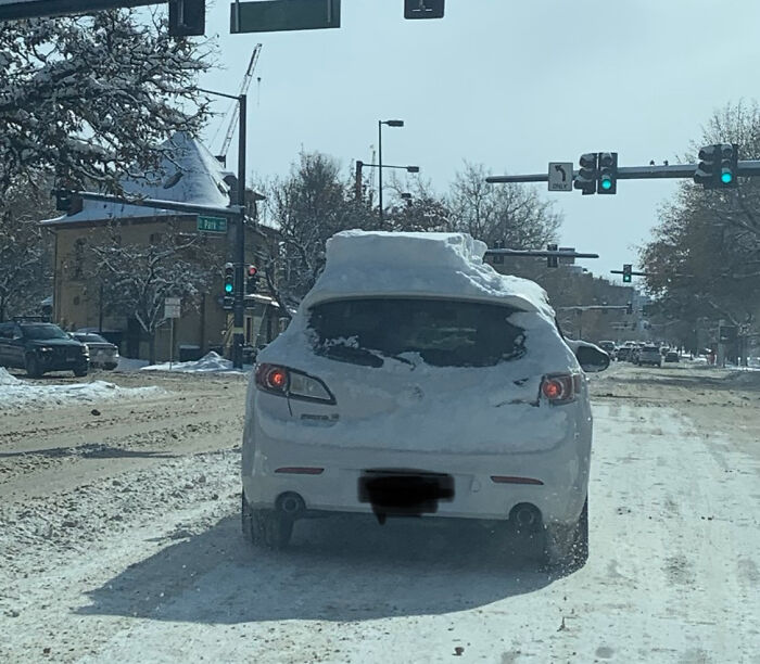 Car with snow-covered rear at a snowy intersection; emphasizing lazy-infuriating-people behavior in winter conditions.