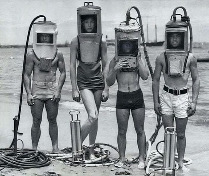 Four people in vintage diving gear on a beach, illustrating historical innovation.