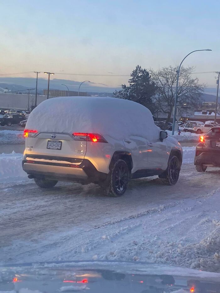 SUV covered in snow driving on a winter road, illustrating lazy-infuriating-people not clearing their cars properly.