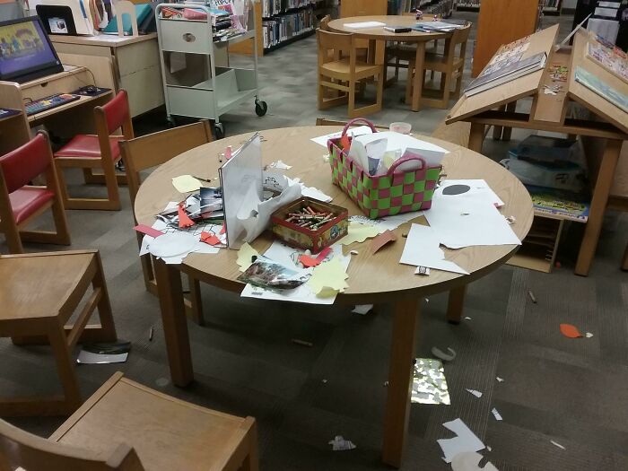 Messy table in a library with papers and craft supplies scattered, illustrating lazy-infuriating-people behavior.