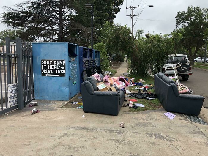 Improperly discarded furniture and trash left in front of recycling bins, highlighting lazy, infuriating behavior.