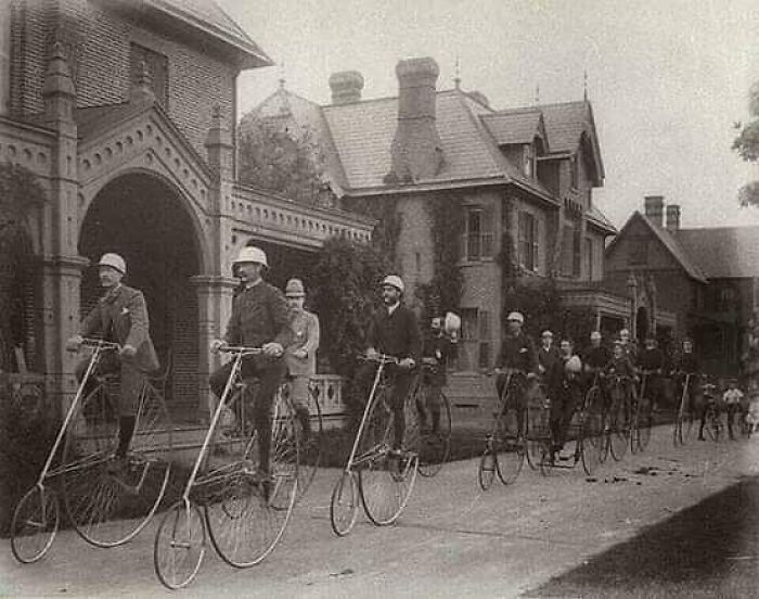 Historical photo of people riding vintage bicycles in front of a large Victorian house, illustrating learning from the past.