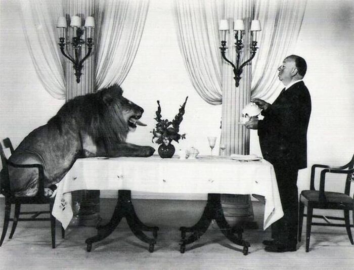 A historical photo of a man serving a seated lion at a dining table in an elegant room.