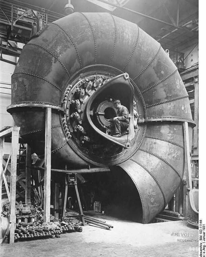 Historical image of a man working inside a large industrial turbine, exemplifying past engineering feats.