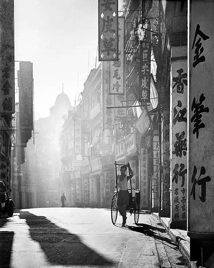 Historical street scene with a rickshaw puller amidst vintage signs and early morning light.