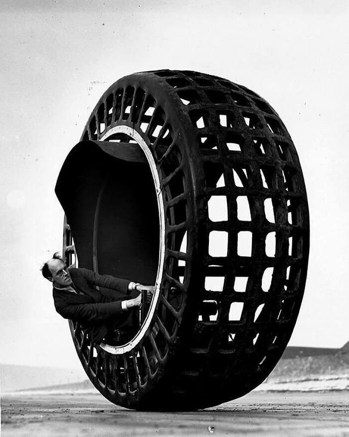 Man seated inside a giant experimental mesh tire, showcasing innovative historical technology and design.