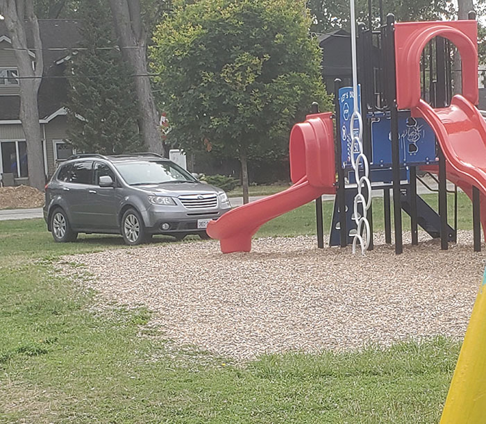 SUV parked on playground wood chips, near red slide, representing infuriatingly lazy behavior.