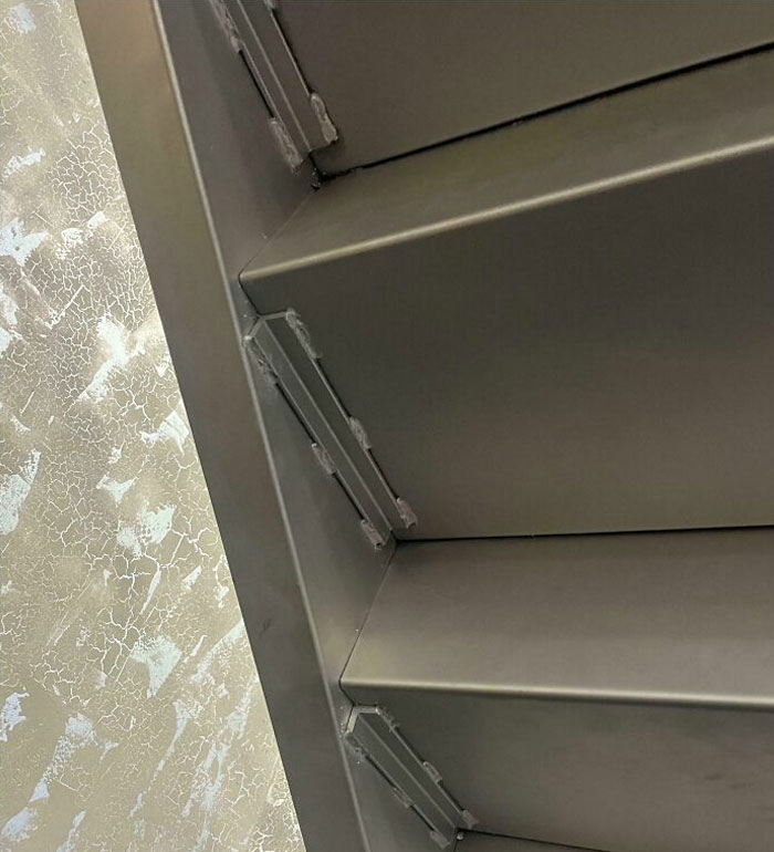 Misaligned metal shelves against a textured wall, illustrating lazy-infuriating-people's handiwork.