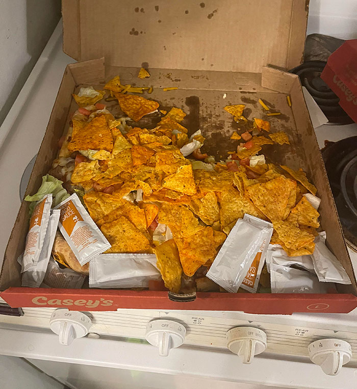 Pizza box filled with nachos and sauce packets on a stove, exemplifying lazy-infuriating people habits.