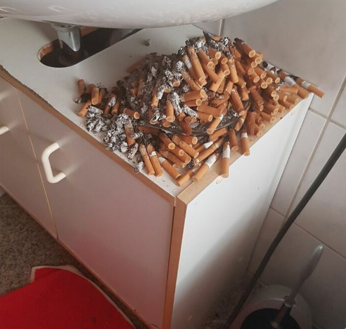 Piles of cigarette butts on a cabinet, showcasing lazy-infuriating habits in a messy bathroom setting.