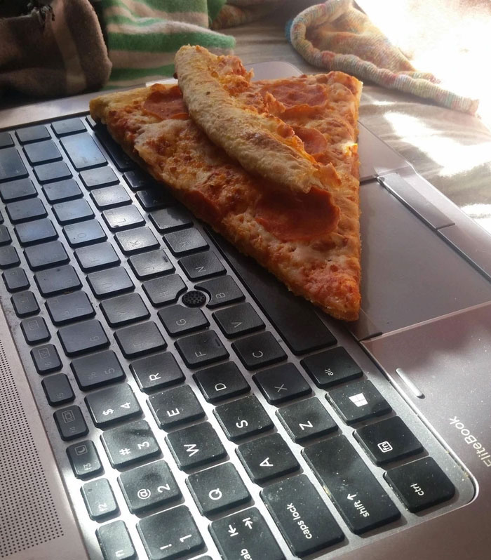 Slice of pepperoni pizza placed on a laptop keyboard, representing lazy-infuriating behavior.