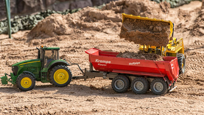 A toy tractor and dump truck in a sandbox, depicting a construction-themed play in a neighbor's yard.