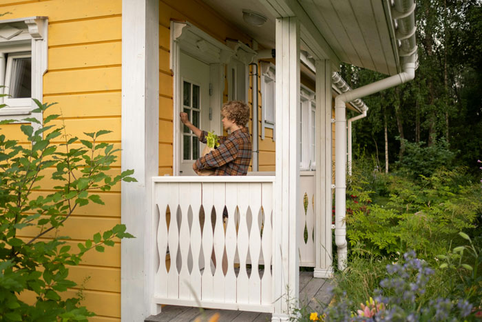 Person knocking on a neighbor's door, surrounded by greenery, in a cozy yard setting.