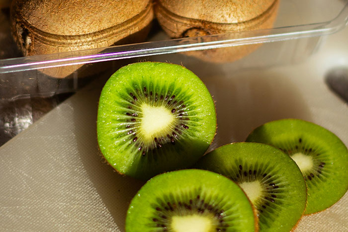 Sliced kiwi fruit with brown skin, showcasing vibrant green and white interior.