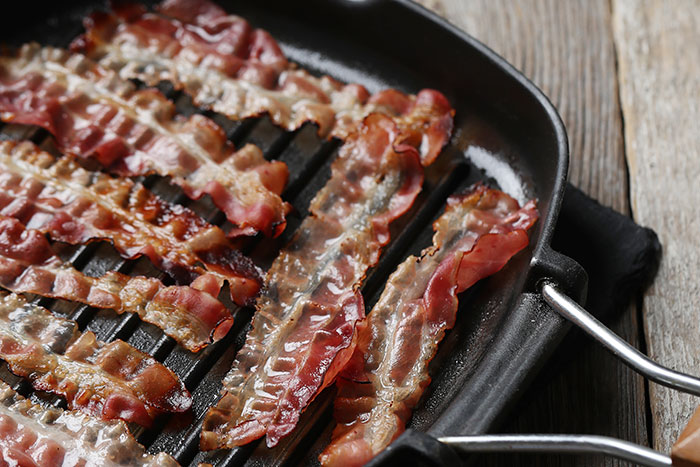 Crispy bacon strips cooking on a grill pan.