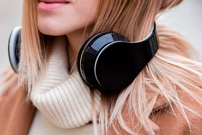 A person wearing large black headphones over a beige sweater, focused on music outdoors.