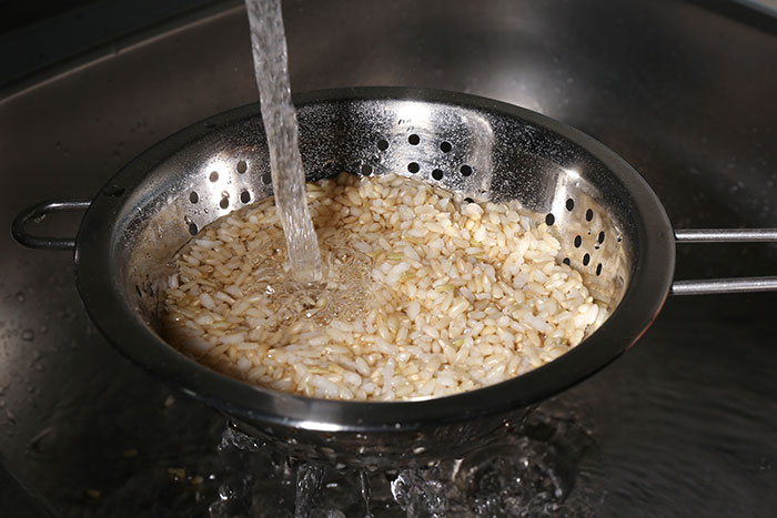 Washing rice in a colander under running water in a kitchen sink.