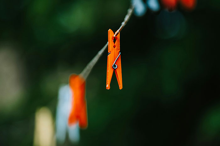 An orange clothespin hangs on a line against a blurred green background.