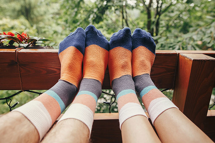 Feet in colorful socks resting on a wooden railing outdoors, with lush greenery in the background.