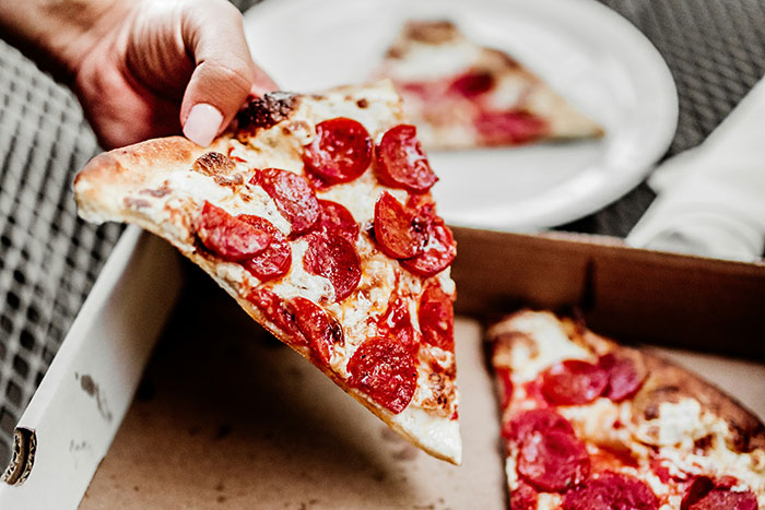 A hand holding a slice of pepperoni pizza over a pizza box.